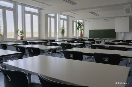 Ein leerer Schulungsraum mit hellen Tischen und schwarzen St&uuml;hlen. Aufstellung in drei Reihen mit jeweils mehreren Tischen hintereinander und jeweils zwei Sitzpl&auml;tzen.